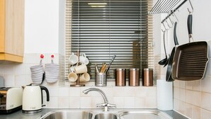 Una cocina con un lavamanos doble, una ventana con persianas y varios utensilios y electrodomésticos.