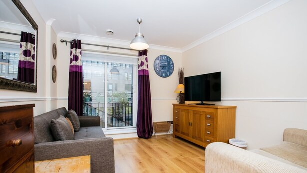 Una sala de estar con sofá, televisor, aparador de madera y ventana con cortinas.