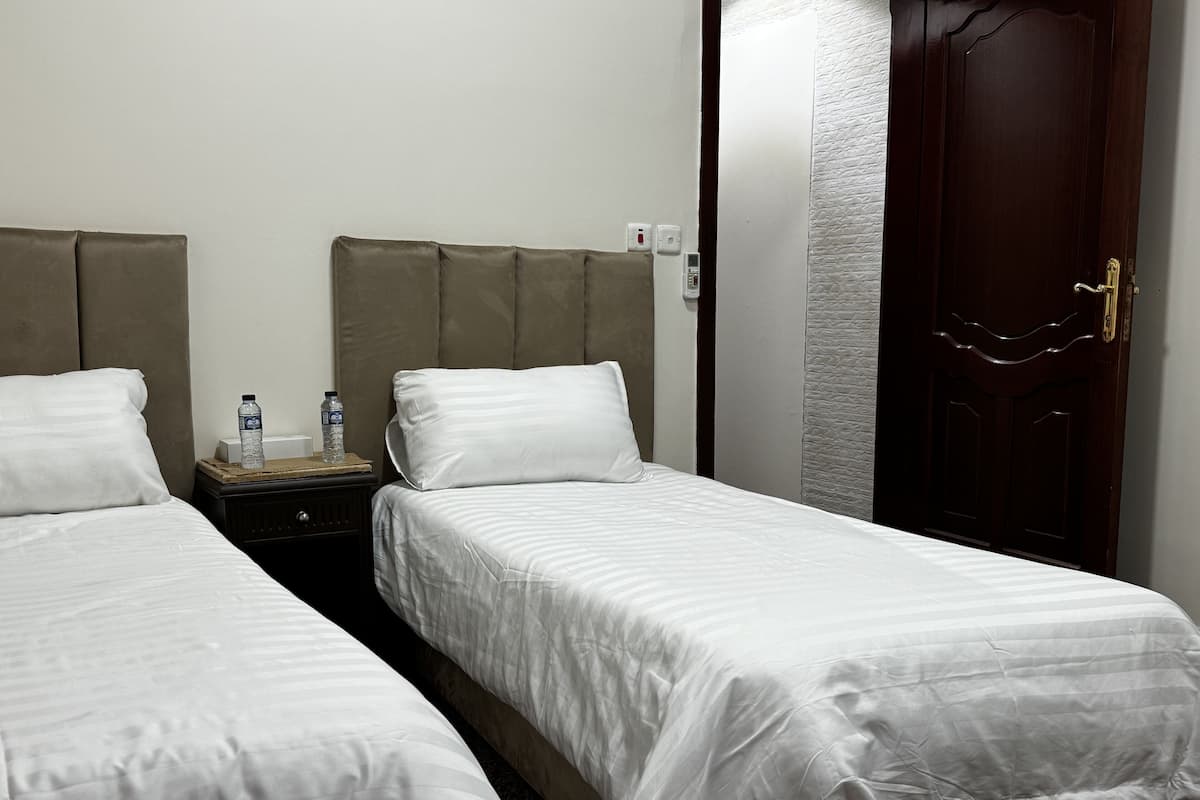 A hotel room with two single beds, a nightstand with a water bottle, and a wooden door.