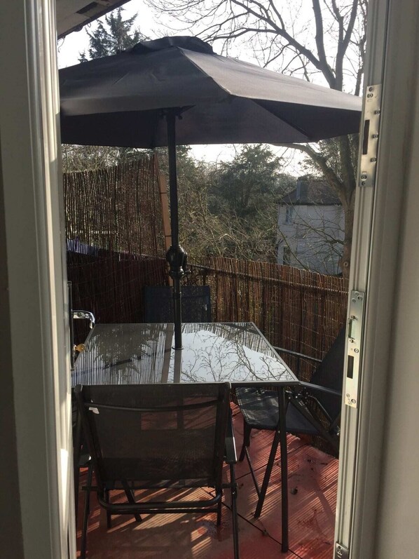Un patio esterno con tavolo e sedie in vetro, un ombrellone grande e un recinto in bambù.