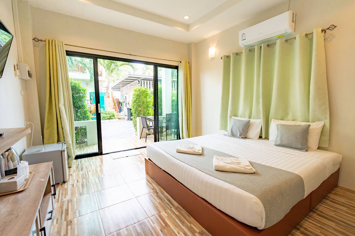 A hotel room with a large bed, a desk with a chair, and a sliding glass door leading to an outdoor area.