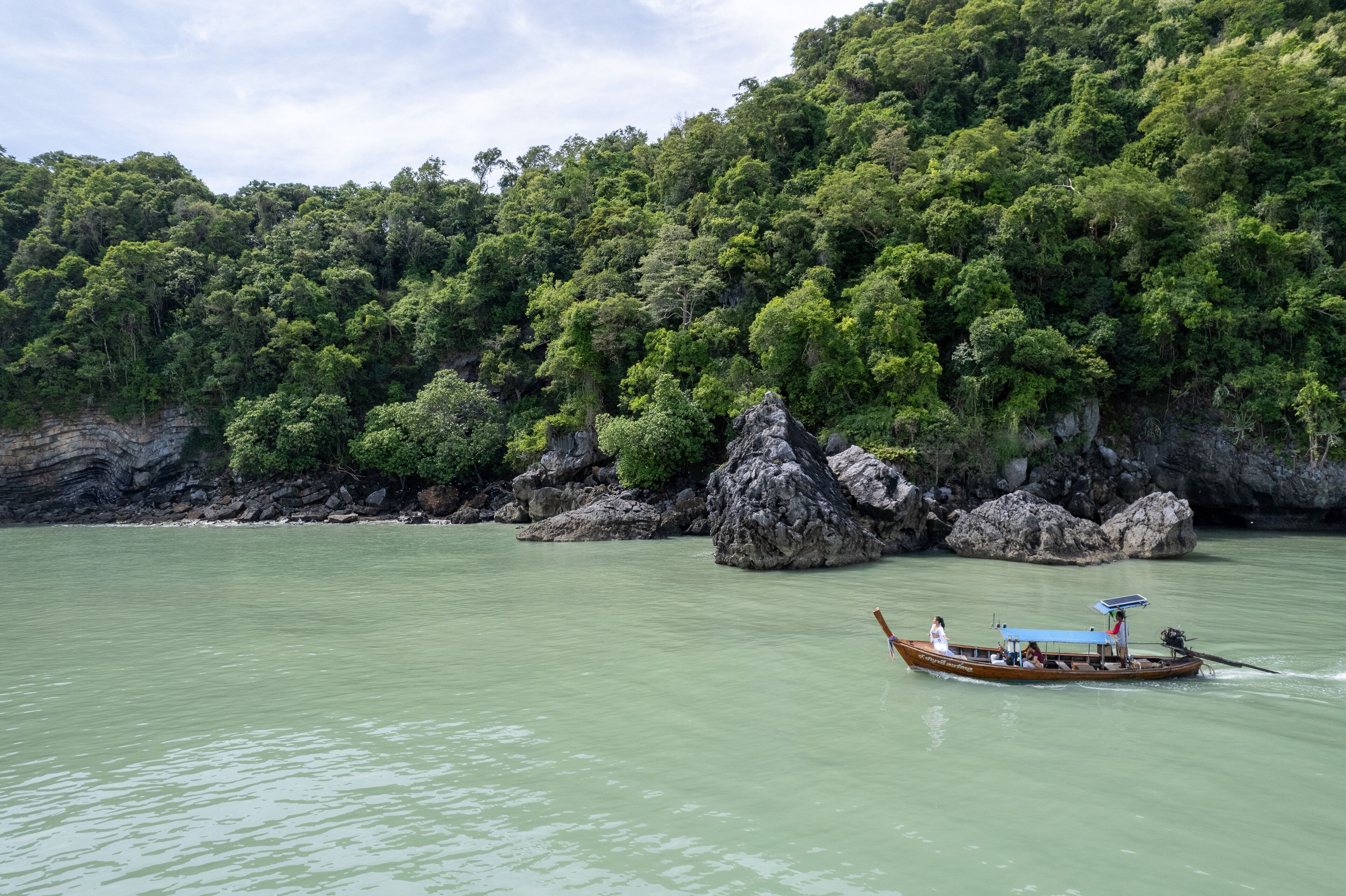 Um barco em um rio calmo, com margens rochosas e uma floresta densa ao fundo.