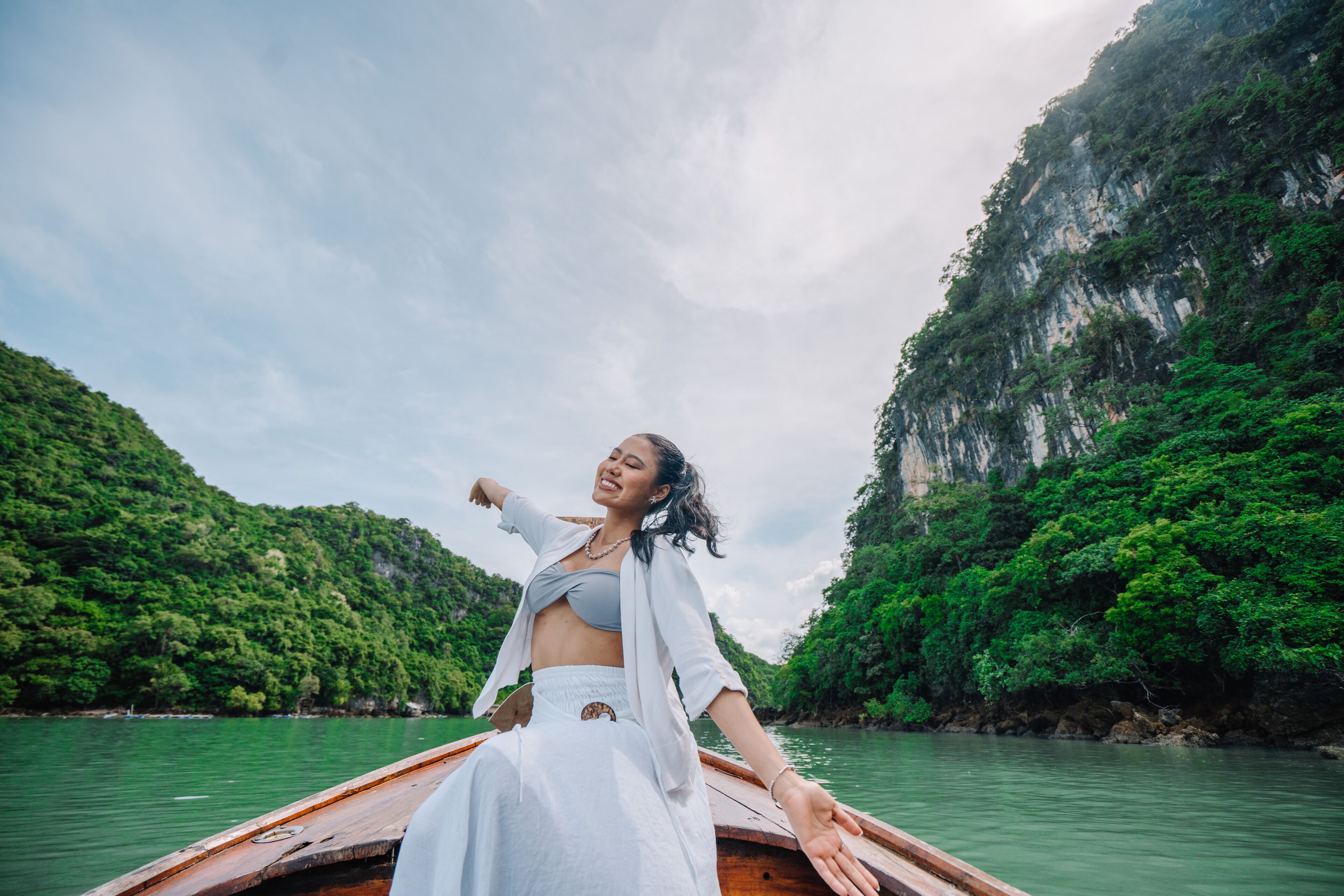 A person on a wooden boat in a river surrounded by lush greenery and cliffs.