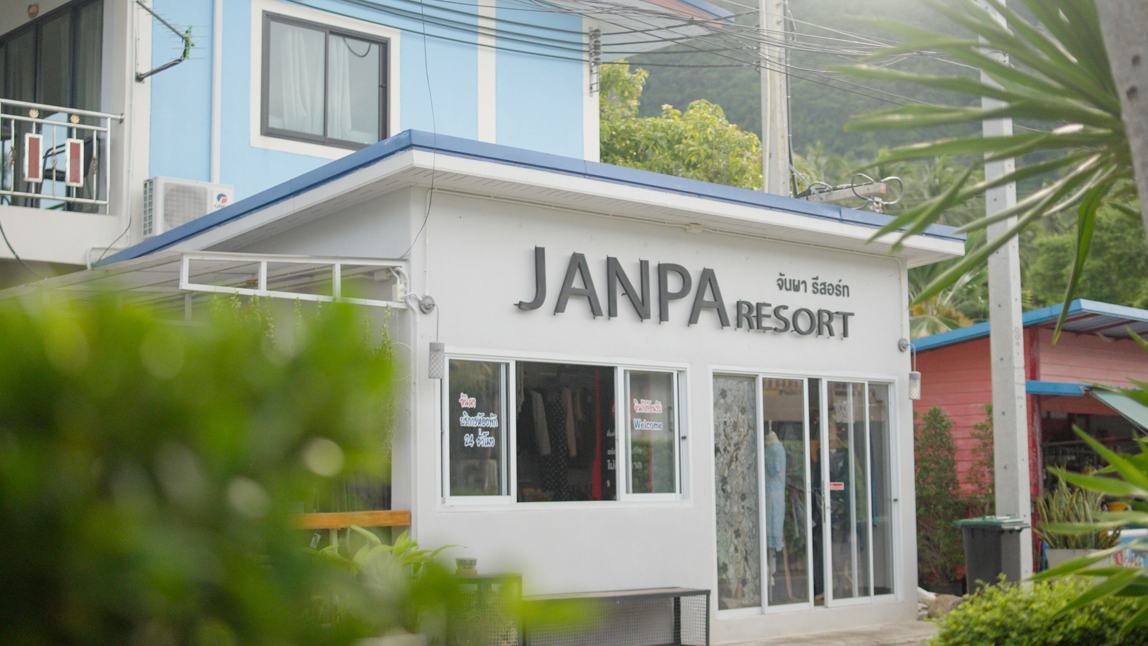 A building labeled "JANPA RESORT" with a white facade, large windows, and a blue roof.