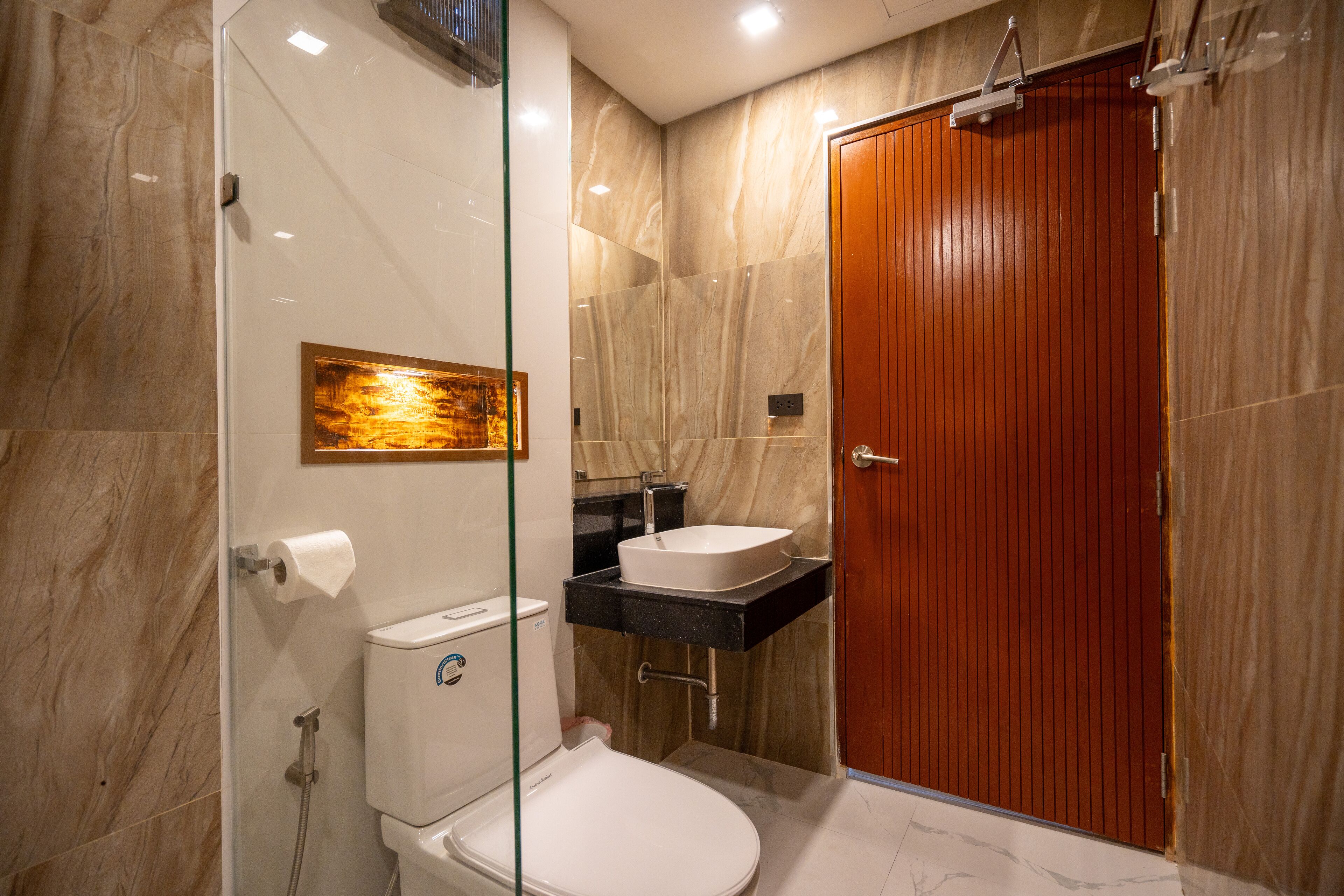 A modern bathroom with a glass shower enclosure, a white toilet, a wooden door, and a marble floor.