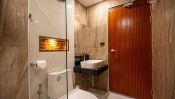 A modern bathroom with a glass shower enclosure, a white toilet, a wooden door, and a marble floor.