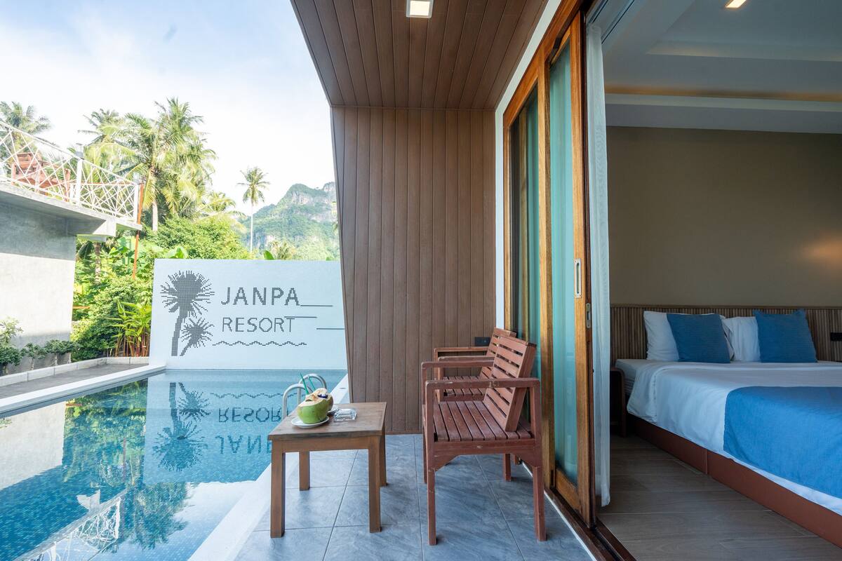 A modern hotel room with a large bed, a wooden table with a bowl, and a view of a swimming pool.