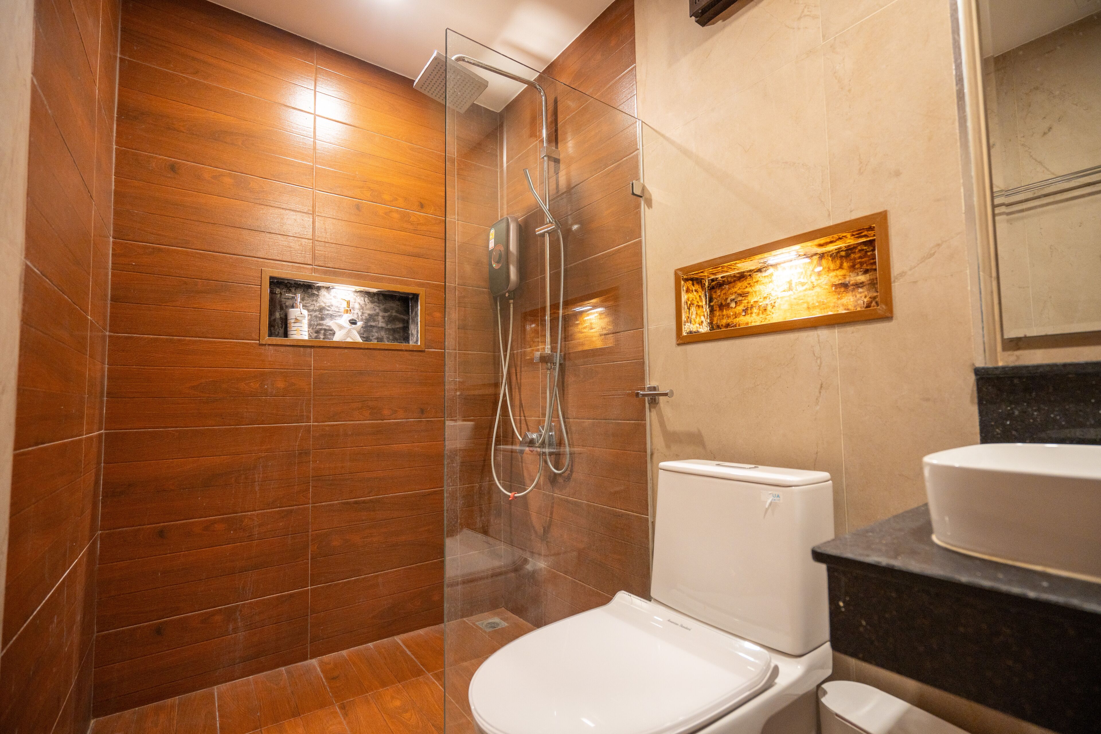 Un baño moderno con pared de madera, ducha con cerramiento de vidrio, inodoro blanco y lavamanos con encimera de mármol.