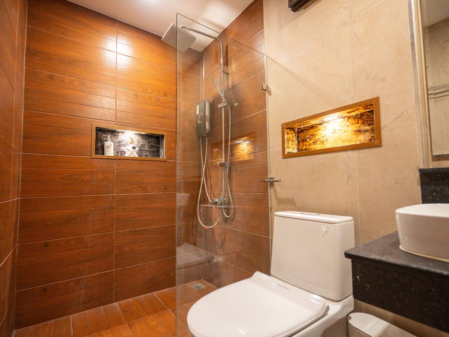 Un baño moderno con pared de madera, ducha con cerramiento de vidrio, inodoro blanco y lavamanos con encimera de mármol.