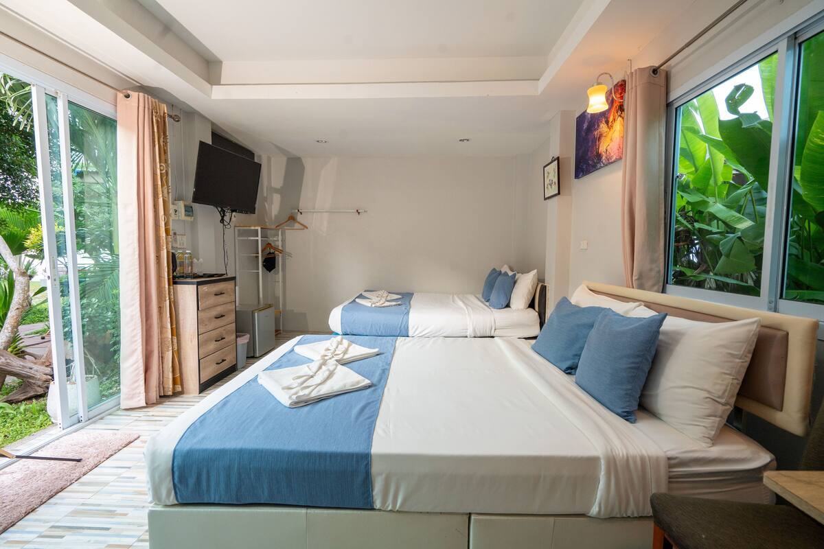 A bedroom with two beds, a TV, and a sliding glass door to a garden.