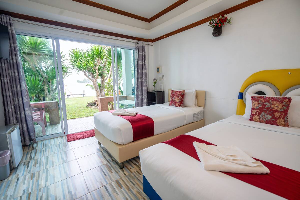 A hotel room with two beds, a sliding glass door to the outdoors, and a small table with a chair.