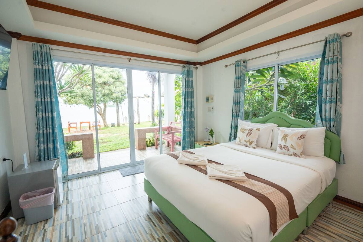A hotel room with a large bed, a desk, and a view of the garden through the sliding glass door.