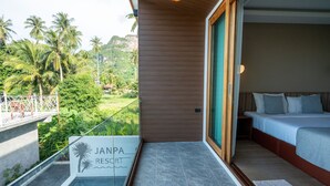 Une chambre d’hôtel avec un lit, un balcon donnant sur des palmiers et une montagne, et une enseigne indiquant « JANPA RESORT ».