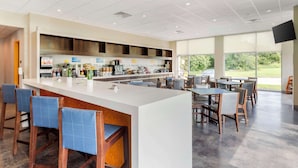 A modern bar area with a long counter, blue cushioned stools, and a seating area with tables and chairs. - GLō Best Western Dallas South DeSoto (DeSoto)