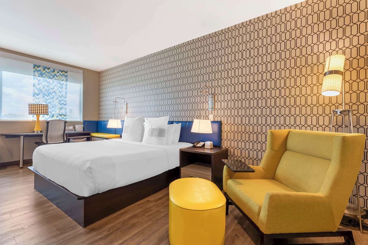A modern hotel room with a large bed, a desk, a chair, and a patterned wall.
