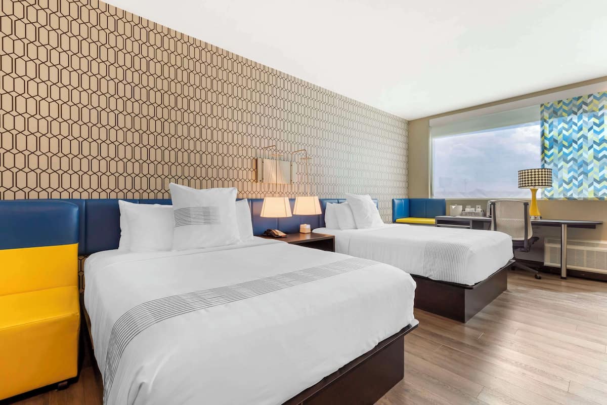 A hotel room with two beds, a desk, and a patterned wall.
