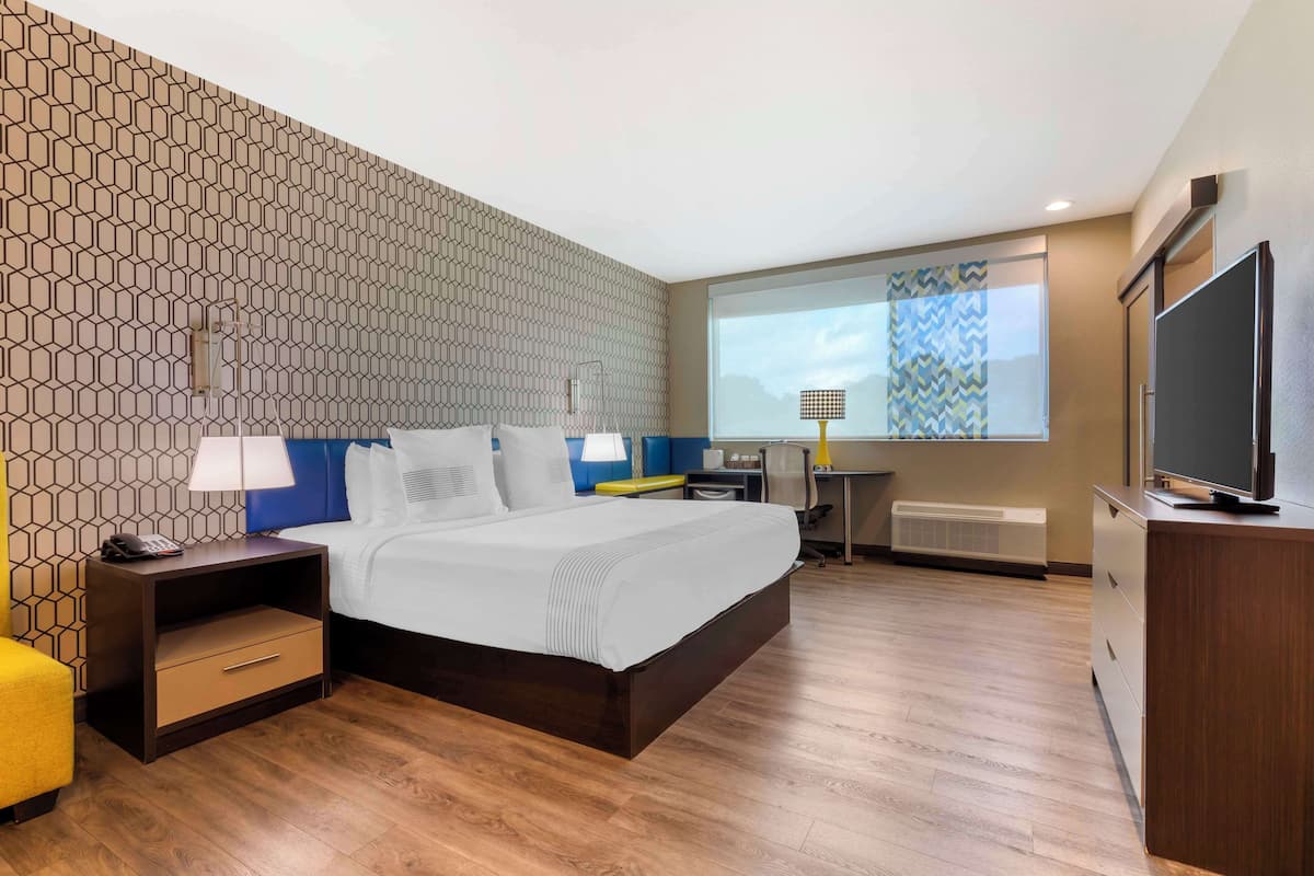 A hotel room with a large bed, a desk, a TV, and a projector screen.