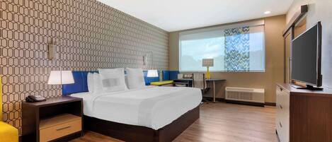 A hotel room with a large bed, a desk, a TV, and a projector screen.