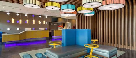 Un vestíbulo moderno con mostrador de recepción, zona de estar y luminarias colgantes de colores.