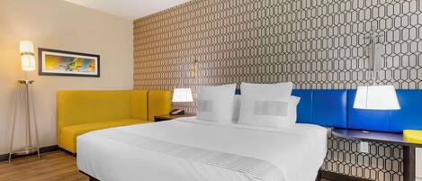 A hotel room with a large bed, a yellow sofa, and a patterned wall.