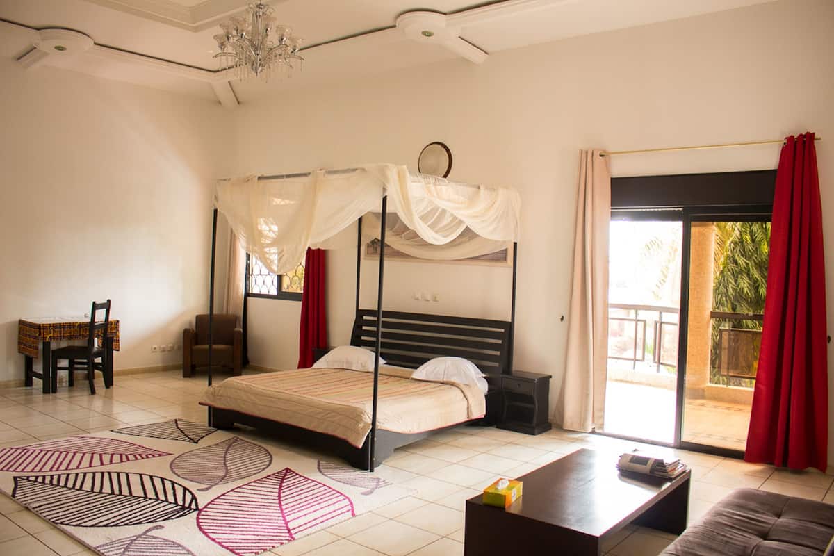 A bedroom with a four-poster bed, a desk, a chair, a sofa, and a view of the outside.
