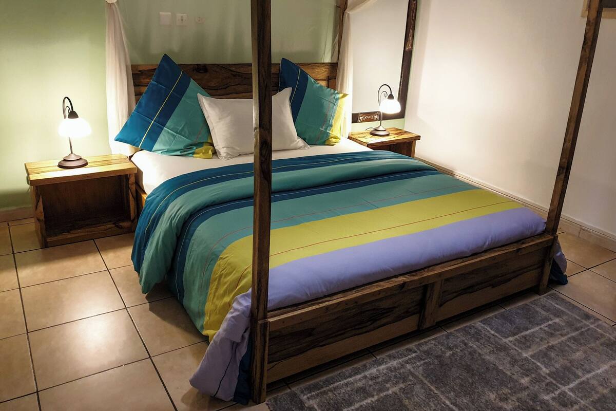 A four-poster bed with a colorful striped bedspread, two nightstands with lamps, and a wooden floor.