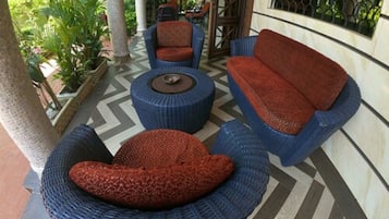 Un espacio de estar al aire libre techado, con muebles de mimbre y piso estampado.