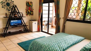 Un dormitorio con una cama, televisor sobre un mueble, refrigerador y una ventana con cortinas.