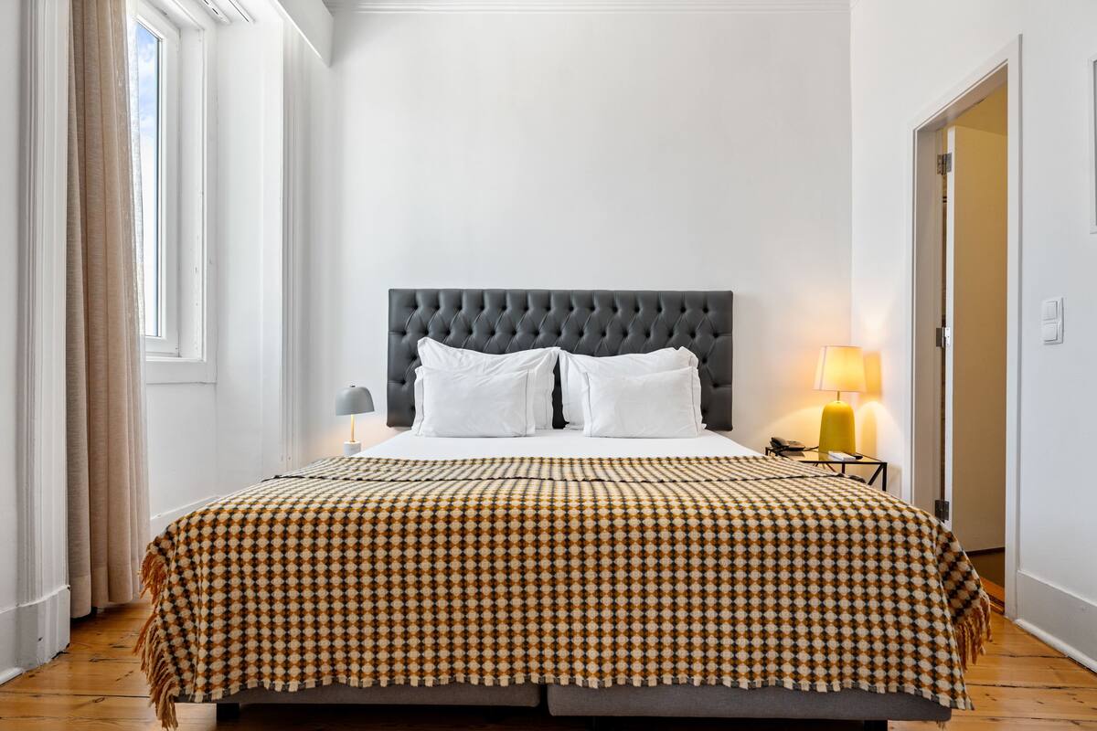 A neatly made bed with a patterned bedspread, a tufted headboard, and a bedside lamp.