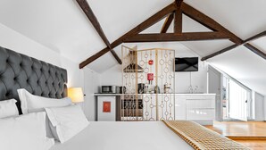 Un dormitorio moderno con una cama grande, una cocina al fondo y un techo alto con vigas a la vista.