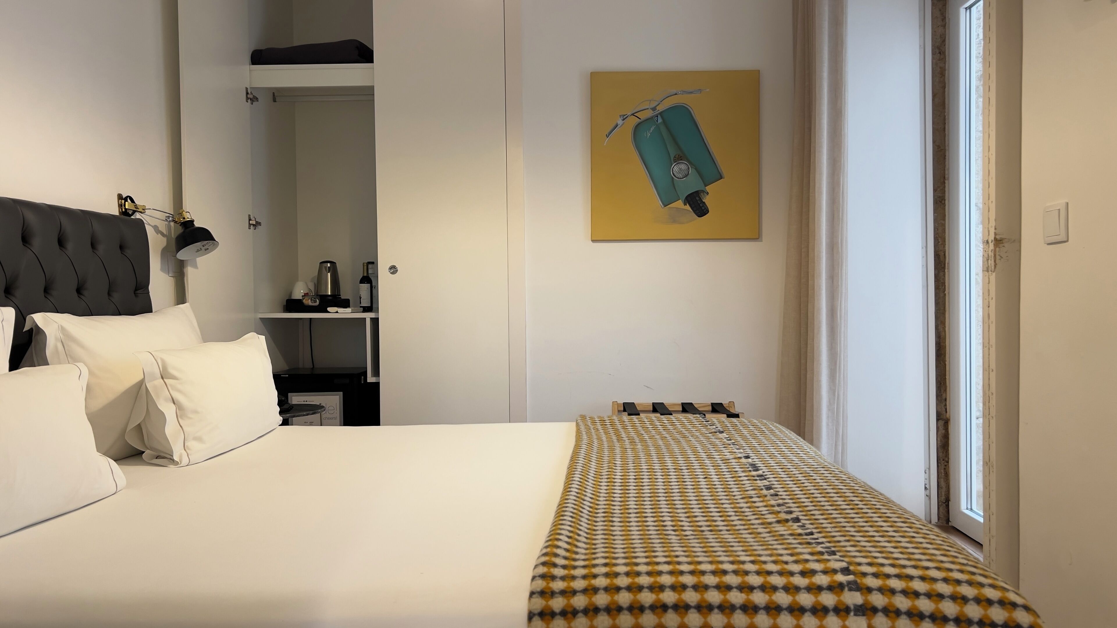 Een netjes ingerichte hotelkamer met een bed, nachtkastje, lamp, kledingkast en een raam met uitzicht.