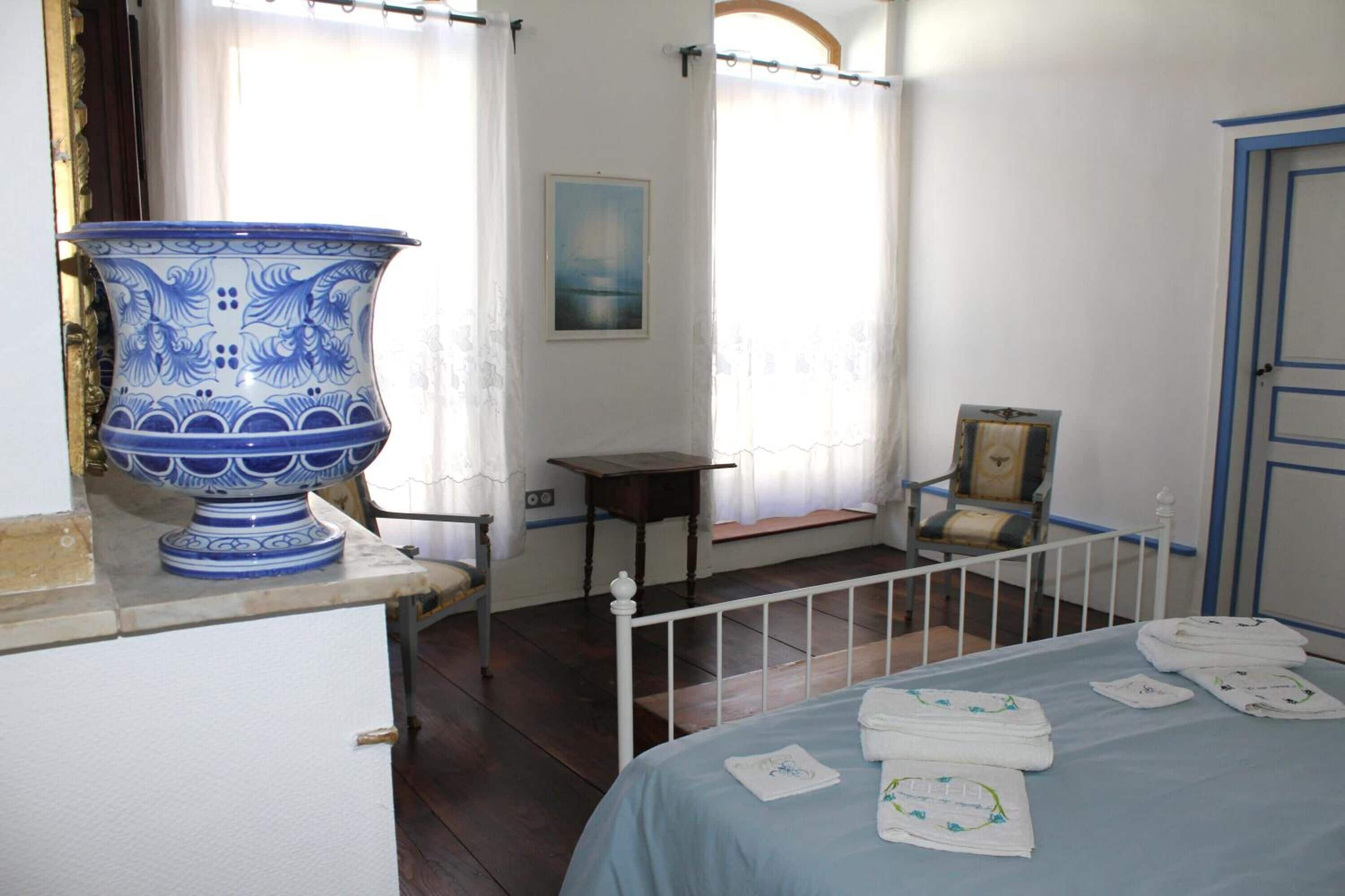 Una habitación con una cama, un cuenco grande de cerámica azul y blanca, una mesita y una silla.