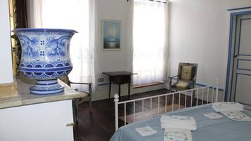 Una habitación con una cama, un cuenco grande de cerámica azul y blanca, una mesita y una silla.