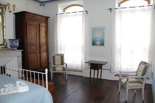 Una habitación con una cama, un armario de madera, una silla, una mesita y dos ventanas con cortinas.