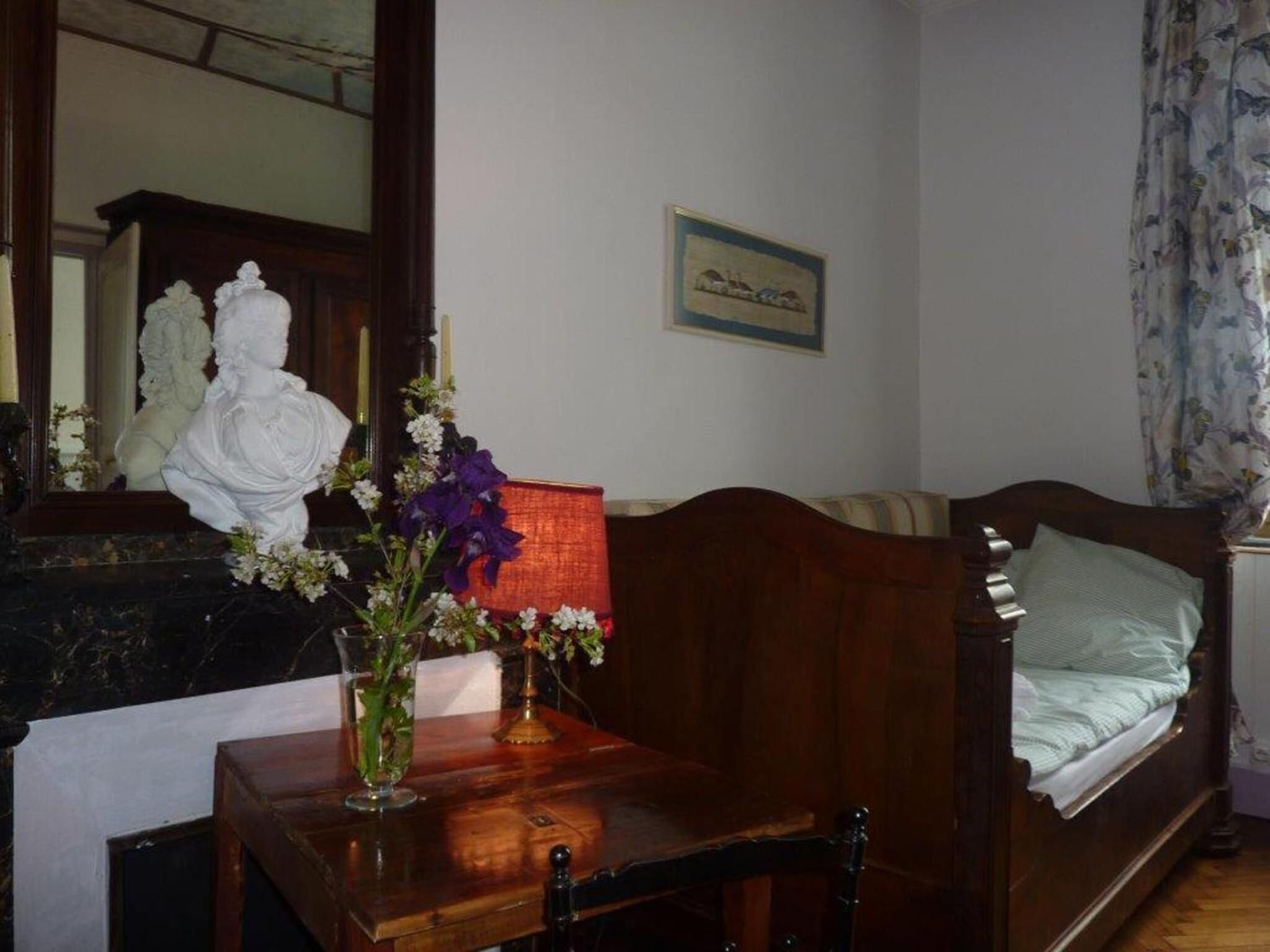 Un dormitorio con una cama de madera, una mesita de noche, un espejo y un florero con flores.