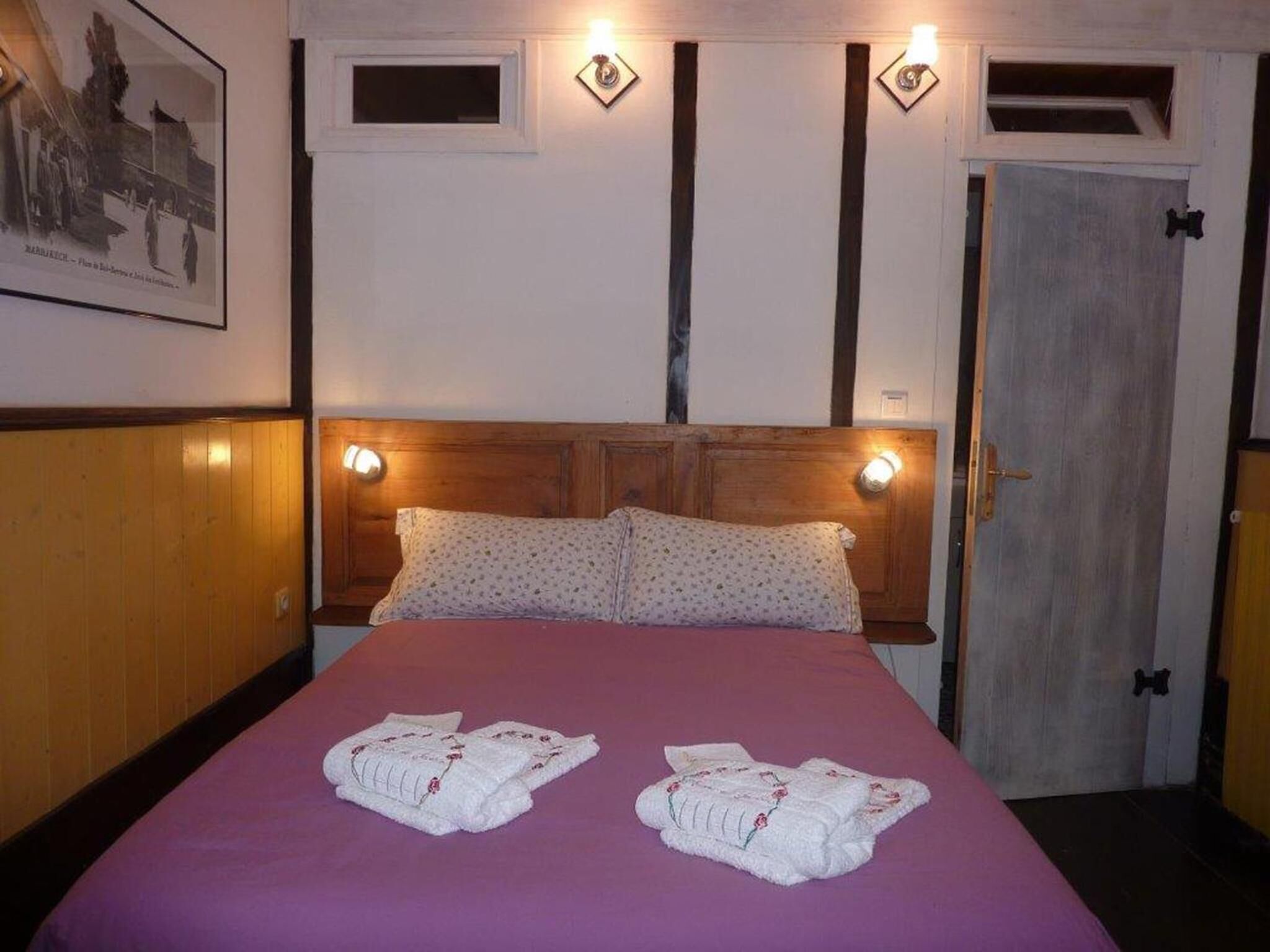 A hotel room with a wooden headboard, two pillows, a purple bedspread, and two towels on the bed.