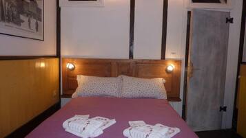 A hotel room with a wooden headboard, two pillows, a purple bedspread, and two towels on the bed.
