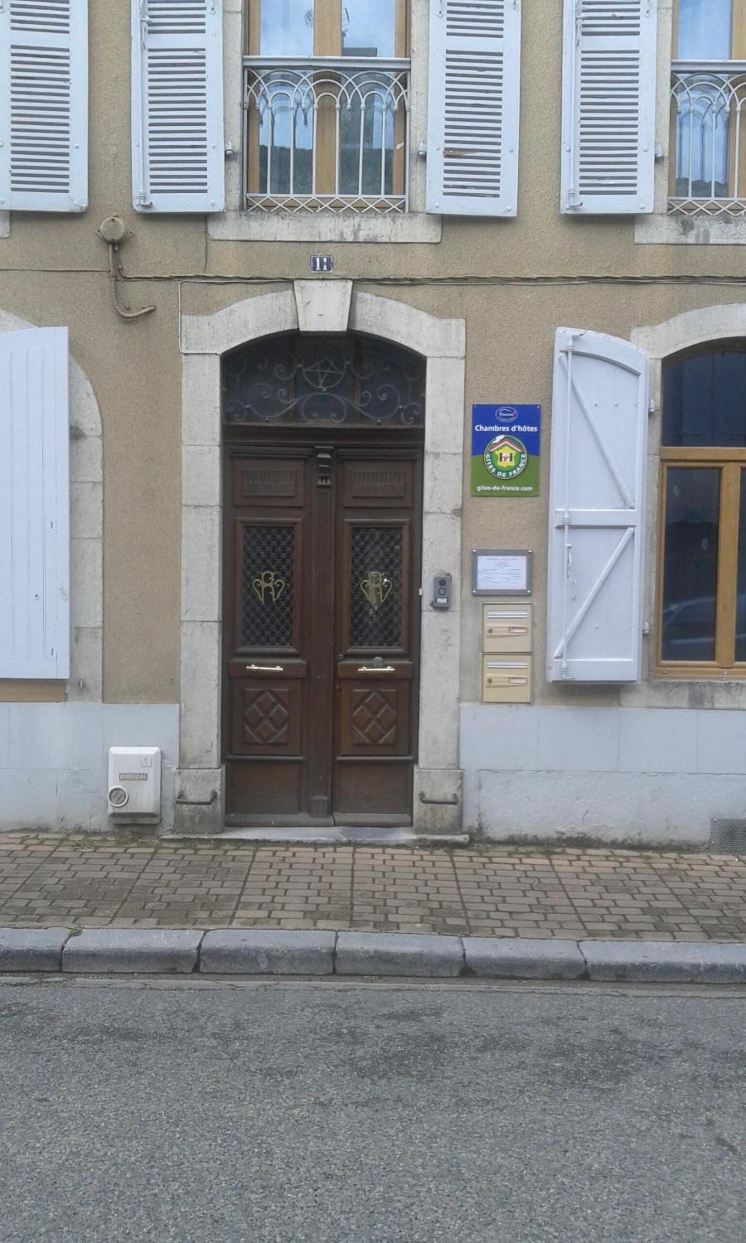A building with a double wooden door, white shutters, and a balcony with metal railings.