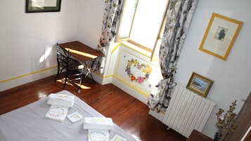 Una habitación con piso de madera, una cama con toallas ordenadas, una silla, una mesa y una ventana con cortinas.