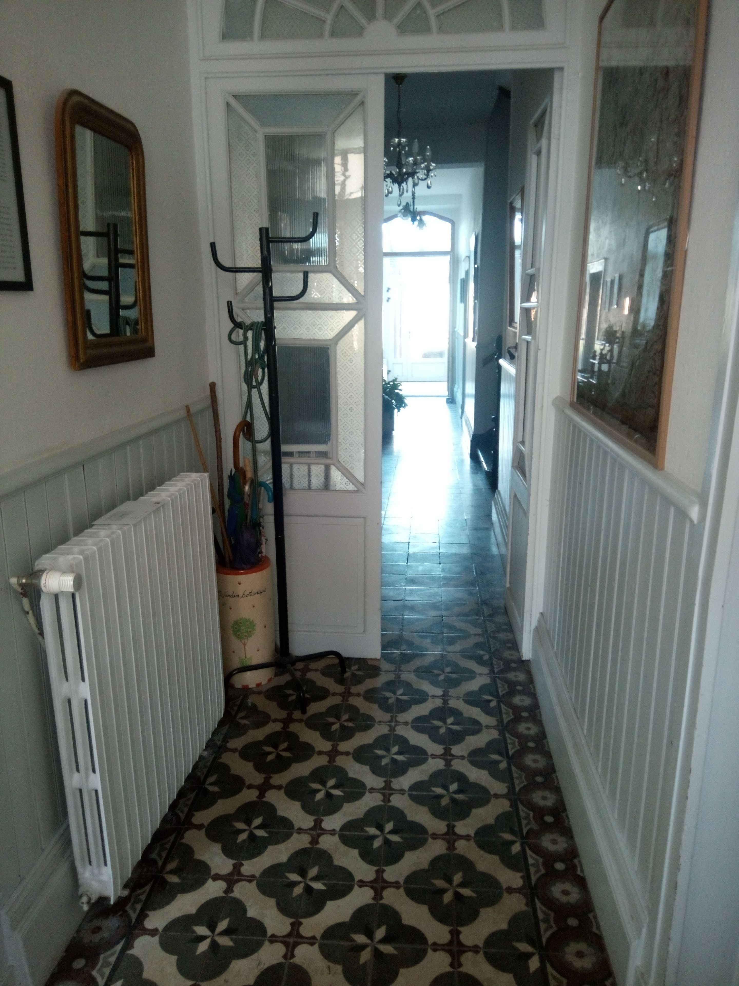 Un pasillo con baldosas de diseño, un radiador, un perchero y una puerta que da a otra habitación.