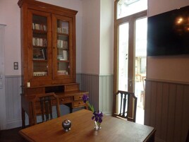 Comedor con mesa de madera, sillas, un aparador con libros y un televisor montado en la pared.