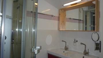 Une salle de bain avec une douche à parois de verre, un meuble-lavabo à deux vasques, un miroir et un porte-serviettes.