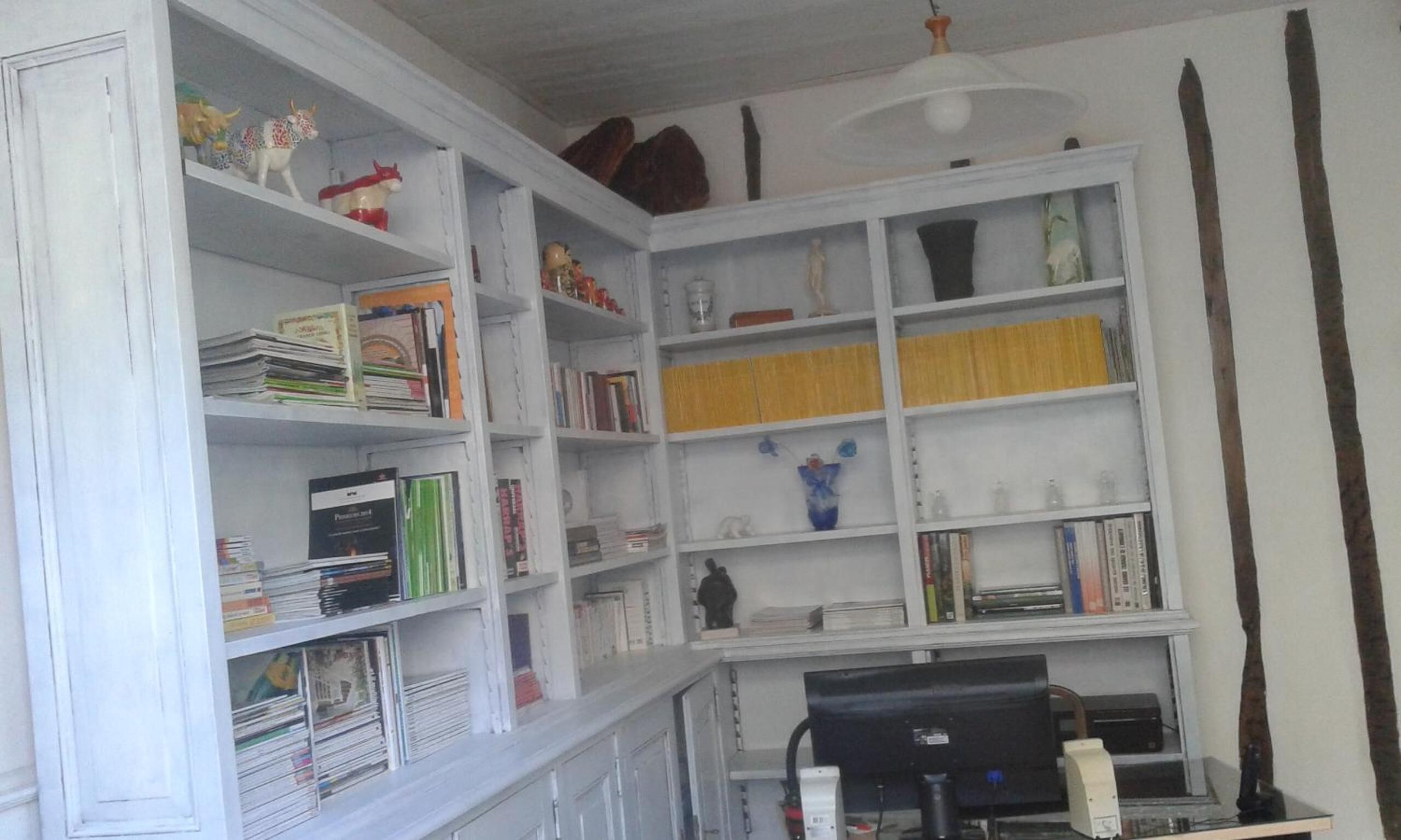 A room with white shelves filled with books and decorative items, a desk with a computer, and a ceiling fan.