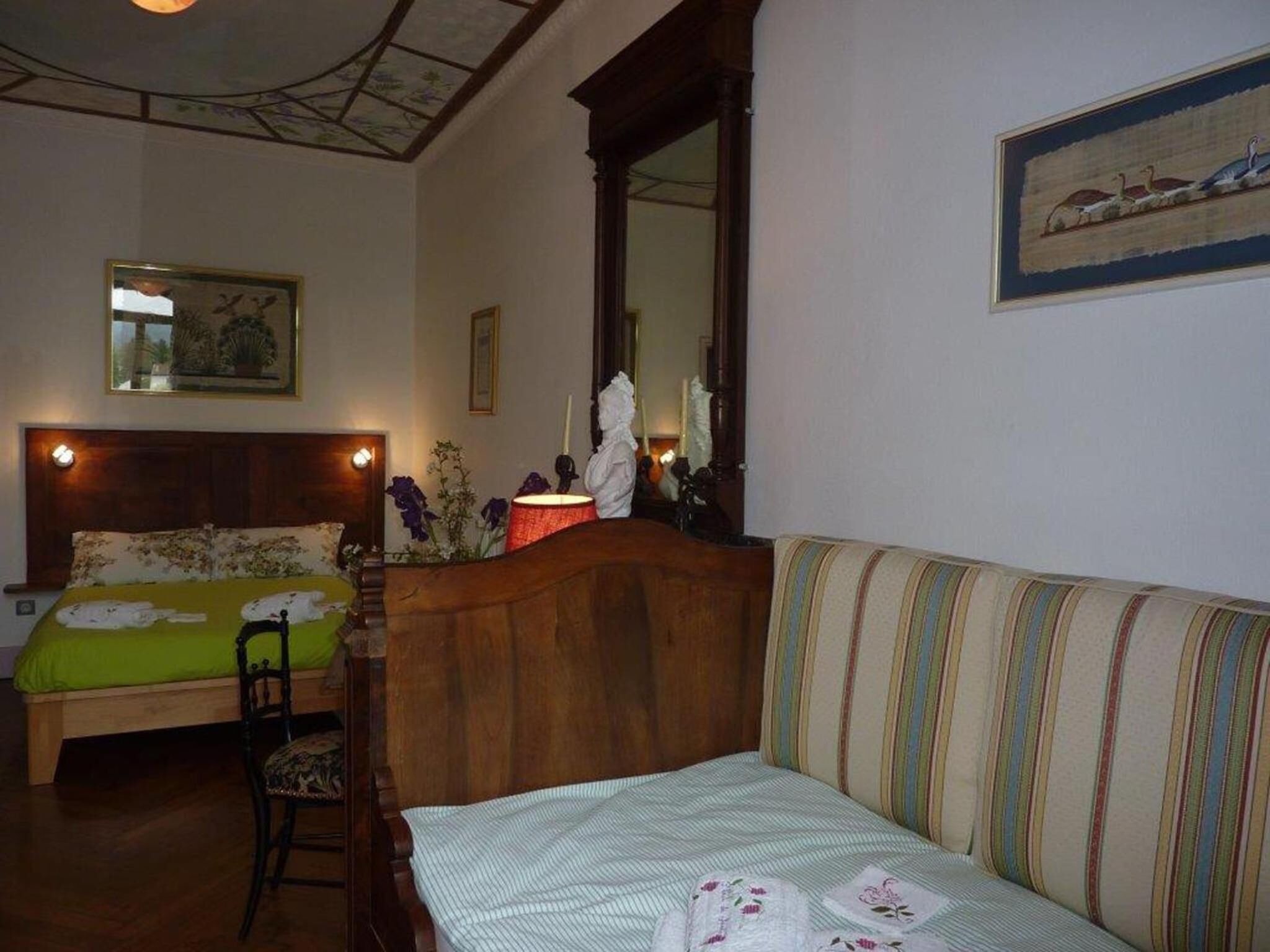 Una habitación con una cama, un sofá, una silla, un espejo y un cuadro en la pared.