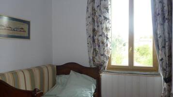 A room with a wooden bed, a window with floral curtains, and a framed picture on the wall.