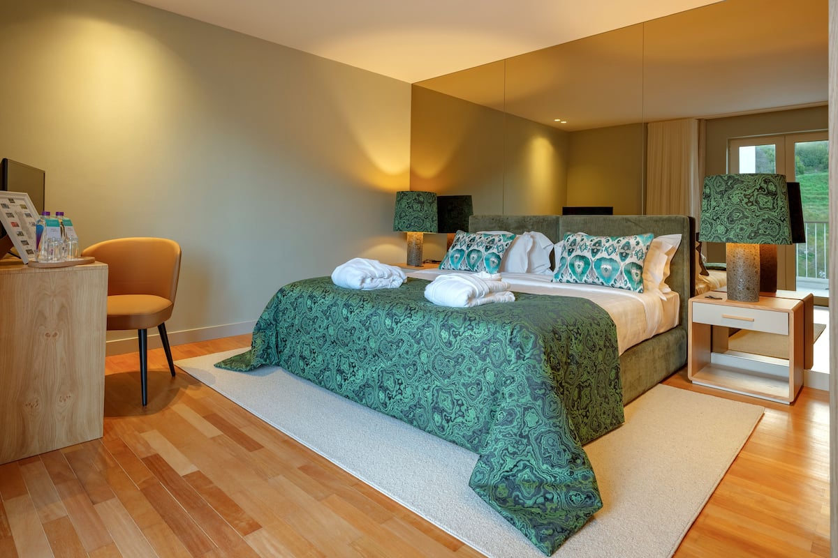 A modern bedroom with a large bed, a bedside table, a chair, and a desk with a lamp.