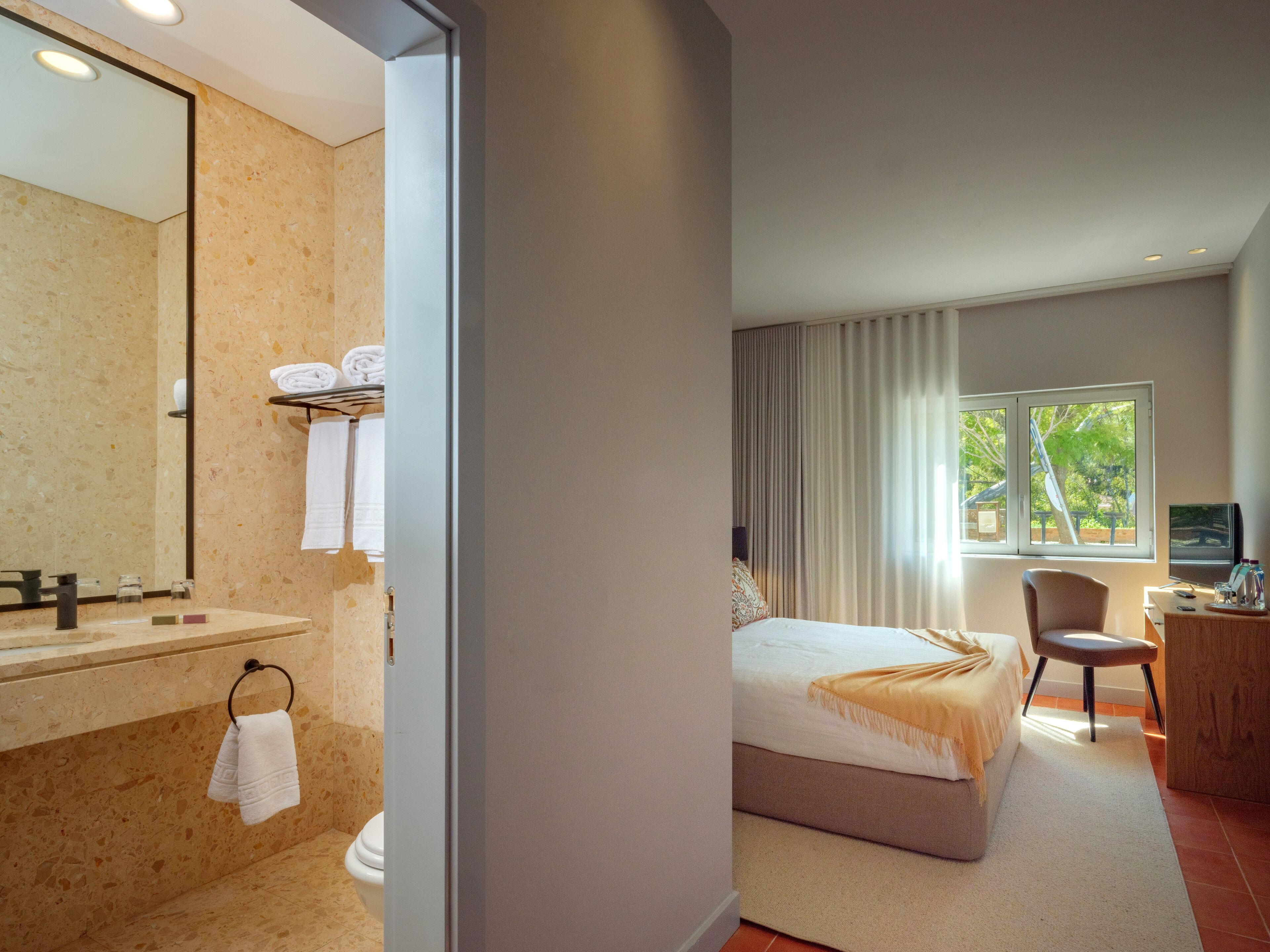 Ein modernes Hotelzimmer mit Bad, Bett, Schreibtisch und Blick ins Freie.