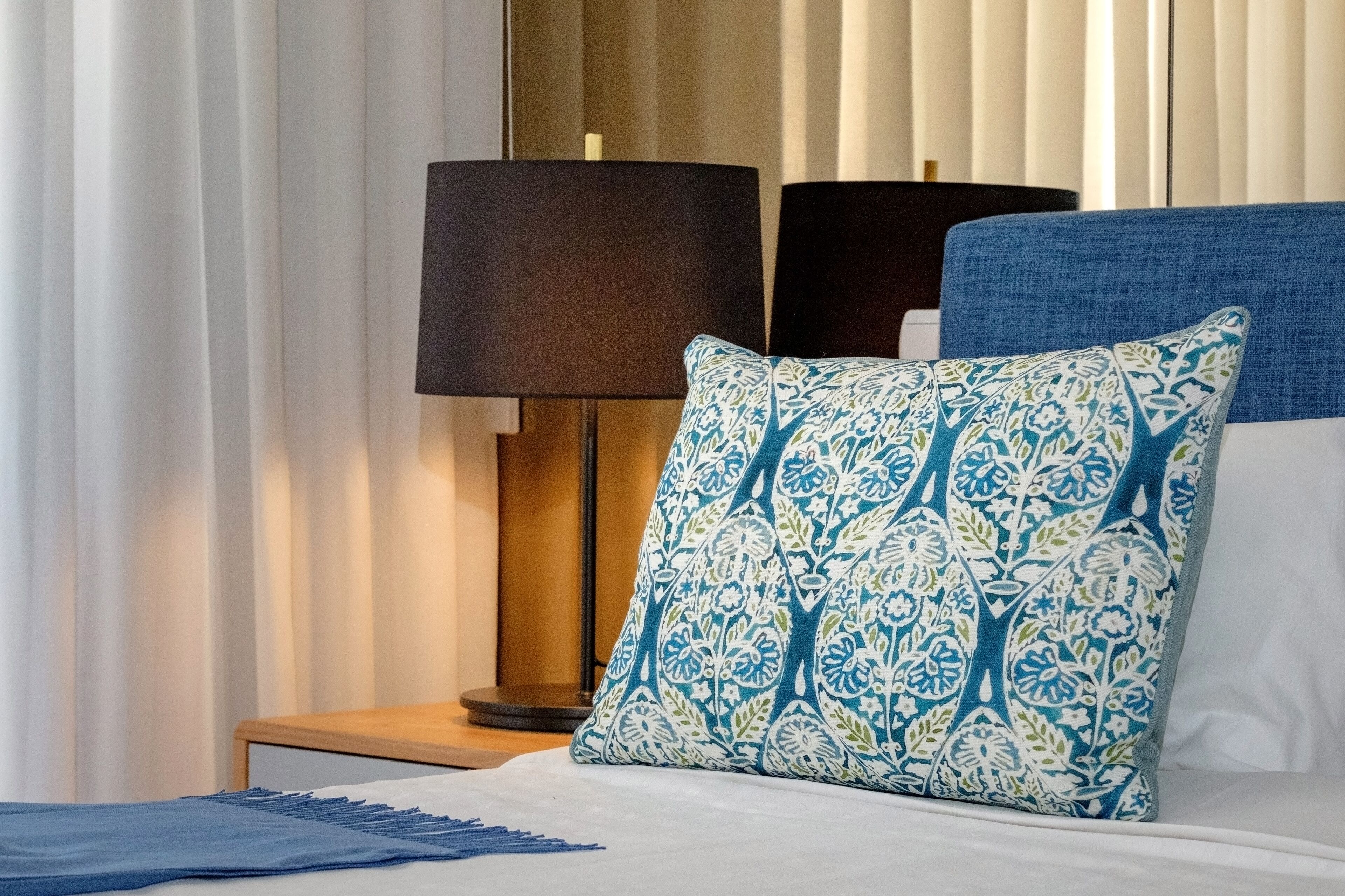 Una habitación de hotel con una cama, una mesita de noche con lámpara y una ventana con persianas.