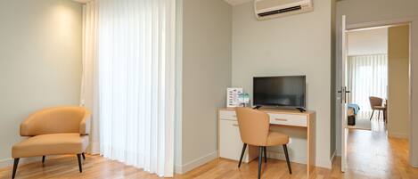 A modern hotel room with a wooden floor, a desk with a computer, a TV, and a chair.