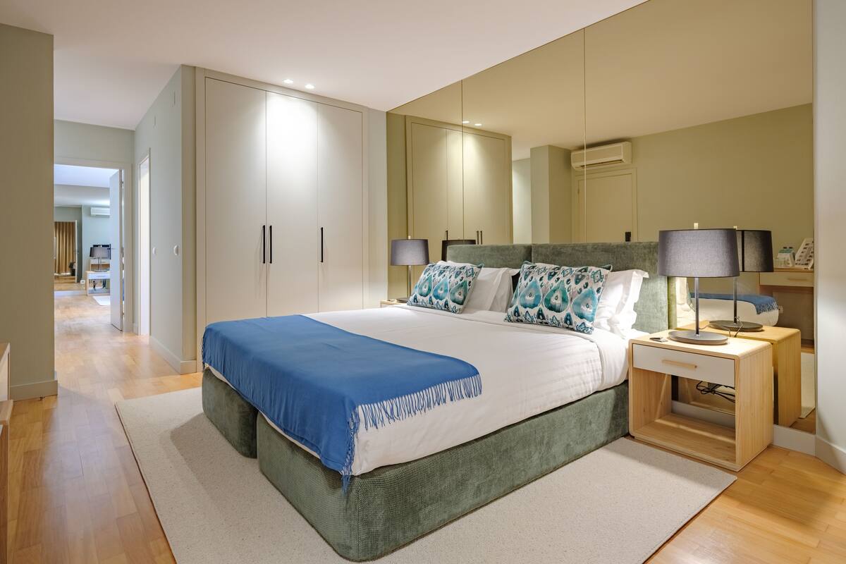 A modern bedroom with a large bed, a nightstand, a mirror, and a wardrobe.